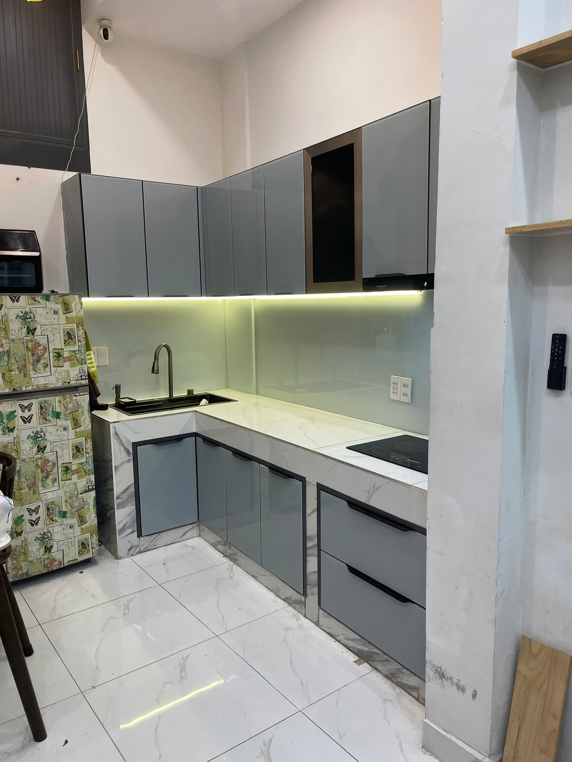 Tủ bếp chữ L cánh kính xám được chụp trực tiếp tại công trình thực tế